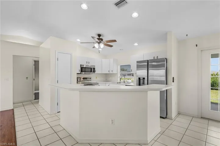 Kitchen featuring light tile patterned flooring, ceiling fan, stainless steel appliances, white cabinets, and a kitchen island