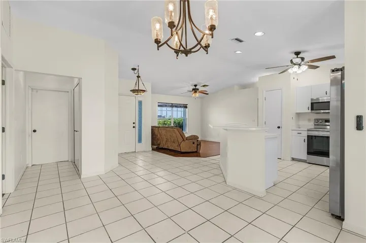 Kitchen with appliances with stainless steel finishes, pendant lighting, light tile patterned floors, ceiling fan with notable chandelier, and white cabinetry