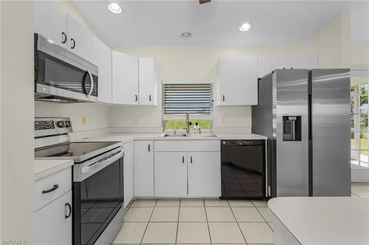 Kitchen with light tile patterned flooring, sink, appliances with stainless steel finishes, and white cabinetry