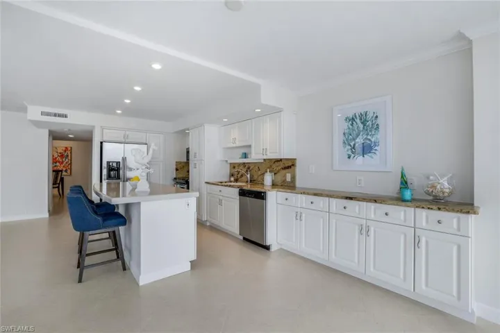 Kitchen with a breakfast bar, appliances with stainless steel finishes, white cabinetry, backsplash, and a kitchen island with numerous cabinets and drawers.