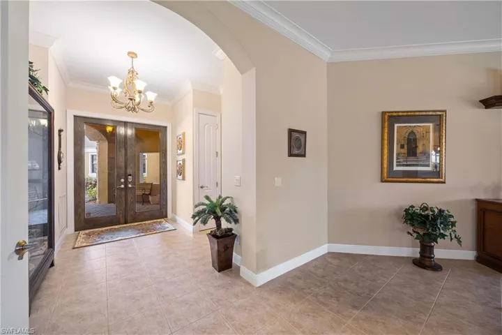 Entrance foyer with arched walkways, ornamental molding, a chandelier, light tile patterned floors, and french doors
