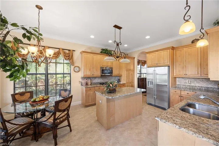 Kitchen featuring appliances with stainless steel finishes, arched walkways, pendant lighting, light stone countertops, and ornamental molding