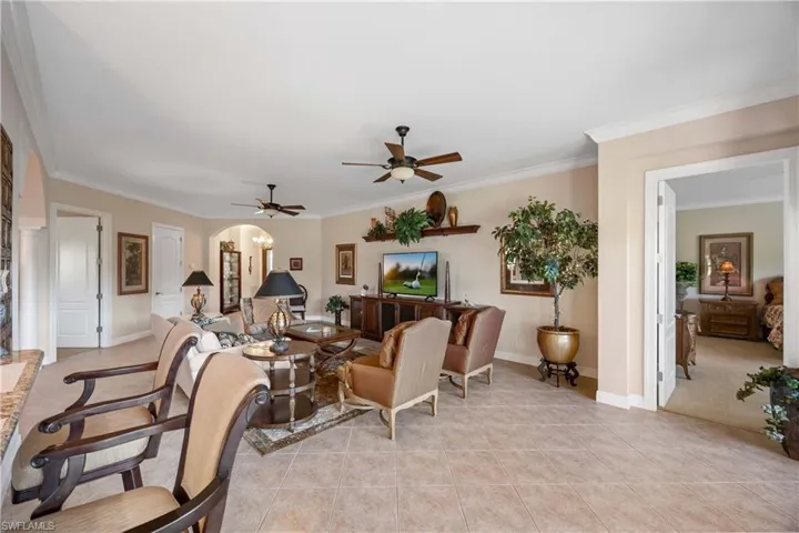 Living room featuring crown molding, a ceiling fan, light tile patterned floors, and arched walkways