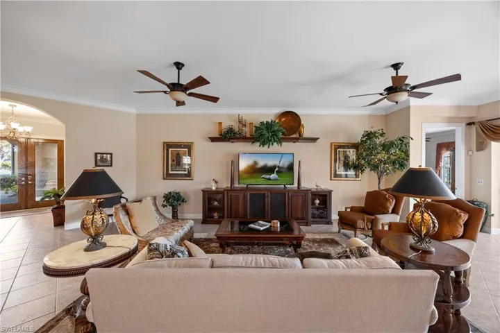 Tiled living room with ceiling fan, ornamental molding, a chandelier, french doors, and arched walkways