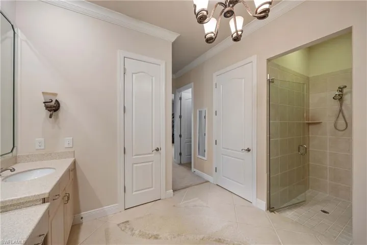 Bathroom featuring vanity, a stall shower, crown molding, a chandelier, and light tile patterned floors