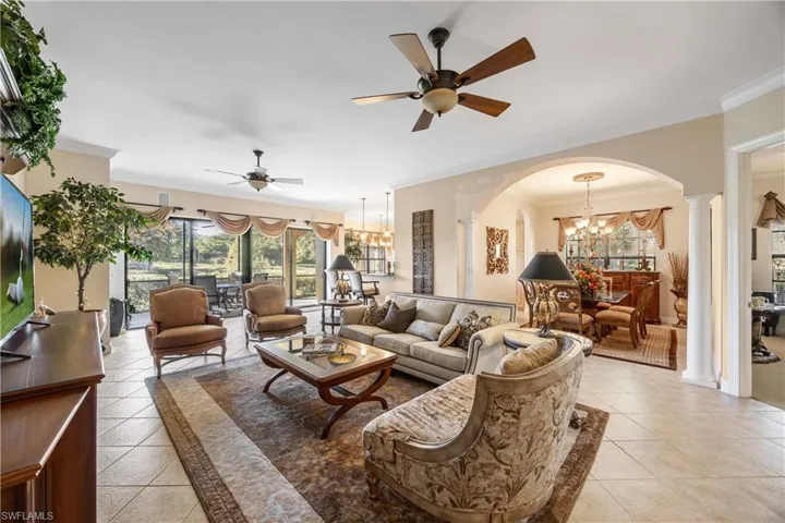 Living area featuring a chandelier, arched walkways, light tile patterned floors, crown molding, and a ceiling fan