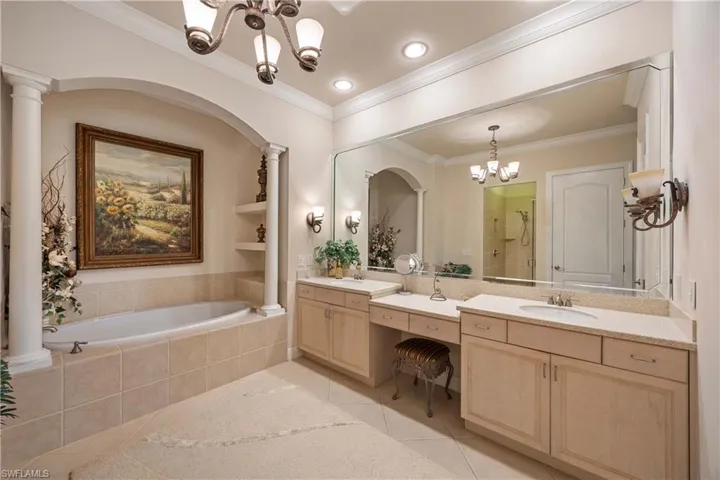 Bathroom with a chandelier, a shower stall, double vanity, crown molding, and decorative columns