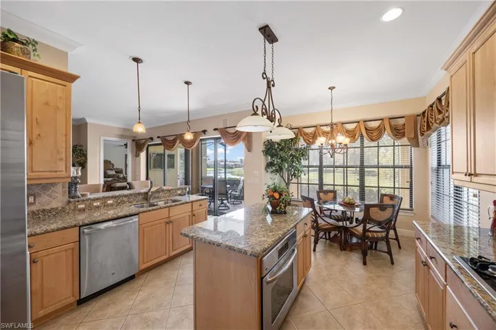 Kitchen with dark stone countertops, hanging light fixtures, stainless steel appliances, crown molding, and light tile patterned floors