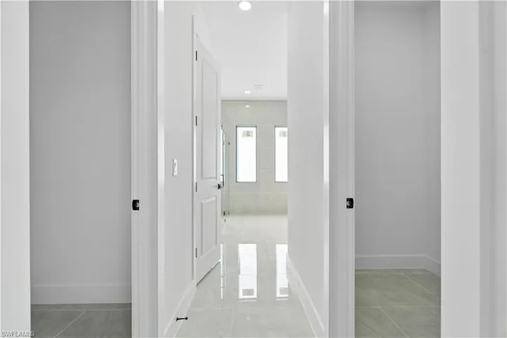 Hallway featuring light gray tile flooring, crisp white walls, recessed ceiling lighting, and a white paneled door with matte black hardware