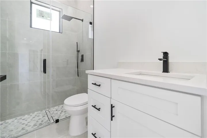Contemporary bathroom featuring a frameless glass shower enclosure, a rain shower head, a built-in shower niche, a white vanity with shaker-style cabinetry, and a countertop with an integrated sink