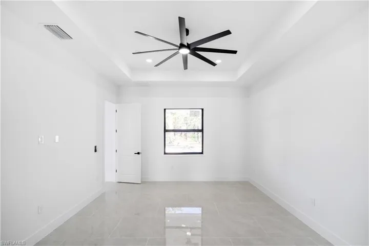 Room featuring large format tile flooring, a tray ceiling, recessed lighting, a ceiling fan, and a single window with dark trim