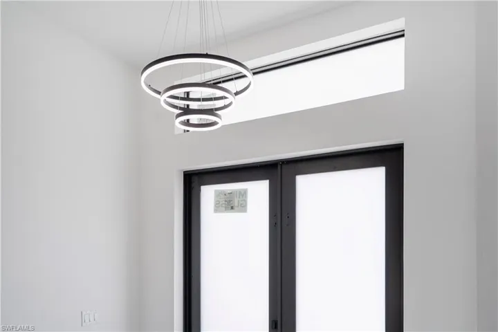 Modern tiered ring chandelier illuminating a white interior with a transom window and a dark-framed double door