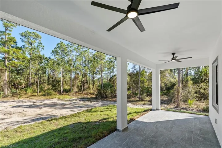Covered patio featuring gray large-format tile flooring, white structural columns, and two black ceiling fans with integrated lighting