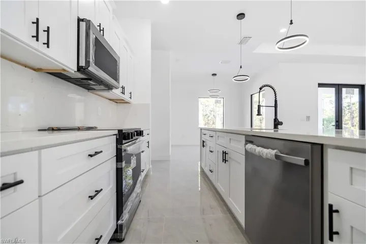 Modern kitchen featuring white shaker cabinetry, stainless steel appliances, a center island with a large sink, and contemporary pendant lighting