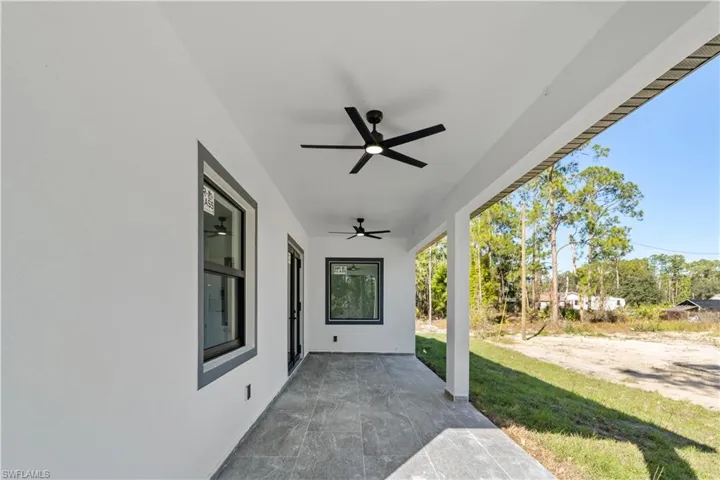 Covered patio featuring two ceiling fans, dark-framed windows, and a glass-paneled door