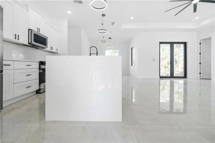 Modern kitchen featuring a large center island with a black gooseneck faucet, white shaker cabinetry with black hardware, stainless steel appliances, and a matching white backsplash