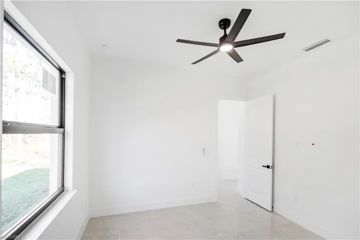 Room with a ceiling fan featuring integrated lighting, large window, white walls, and light-toned tile flooring