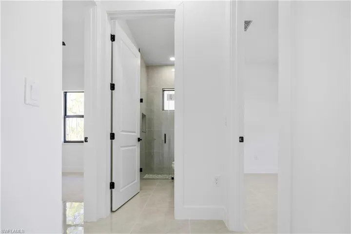 Hallway with light-toned tile flooring throughout, white walls, and white interior doors with black hardware