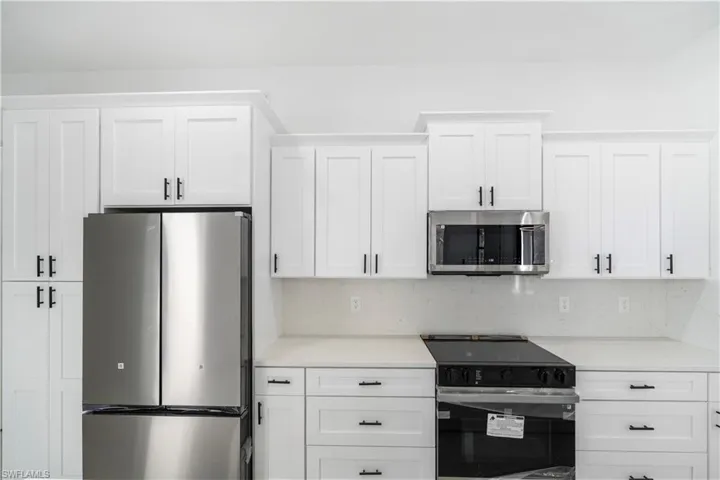 Kitchen featuring white shaker-style cabinetry with matte black hardware, stainless steel appliances, a built-in microwave, and light-toned countertops