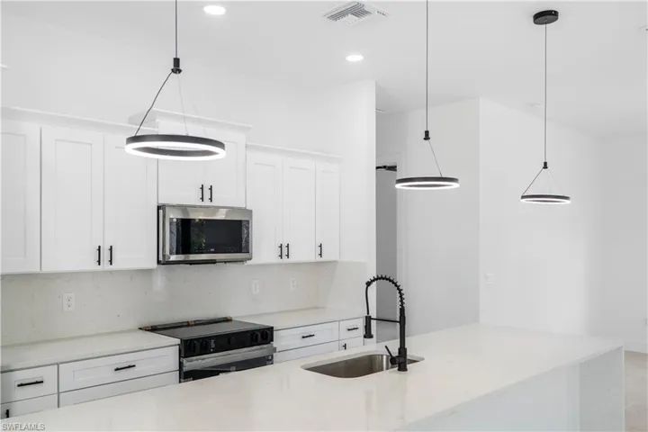 Kitchen featuring white shaker-style cabinetry with black hardware, stainless steel microwave, black range, and light-toned countertops