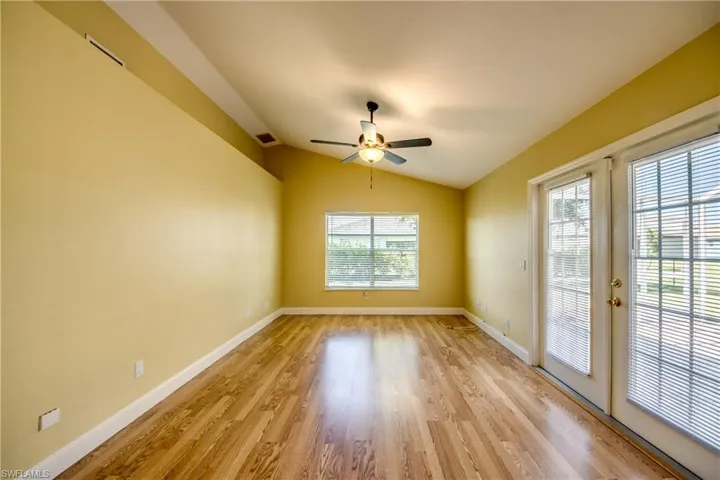 Spacious living room with light wood-type flooring, vaulted ceiling, smart home capable ceiling fan, plenty of natural light, and a set of beautiful white French doors that access oversized patio.