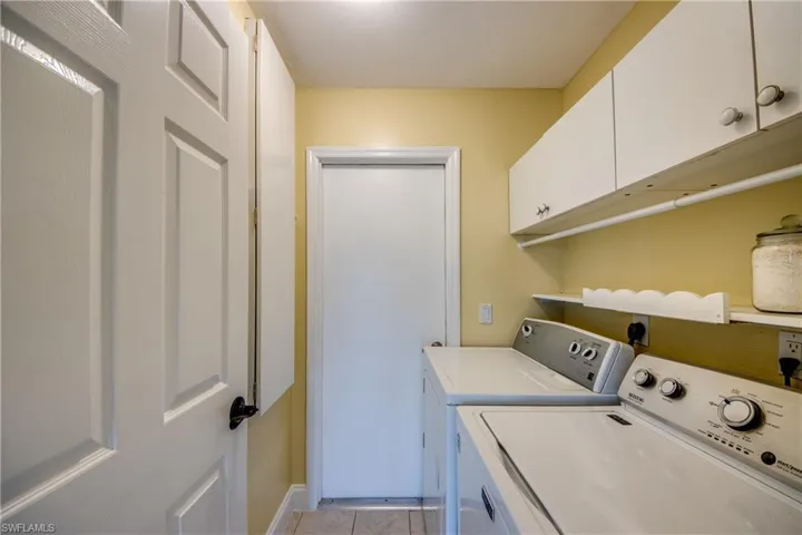 In-house laundry room featuring cabinets, light tile flooring, built-in ironing board, and washing machine and clothes dryer.