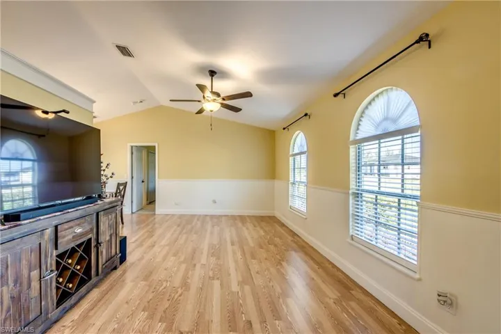 Expansive family room with light wood-type flooring, arched windows, smart home capable ceiling fan, and lofted ceiling.