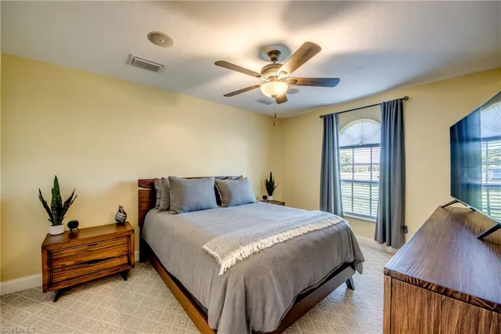 Master bedroom with light colored farmhouse-style carpeting, plenty of natural light from arched window, and smart home capable ceiling fan.