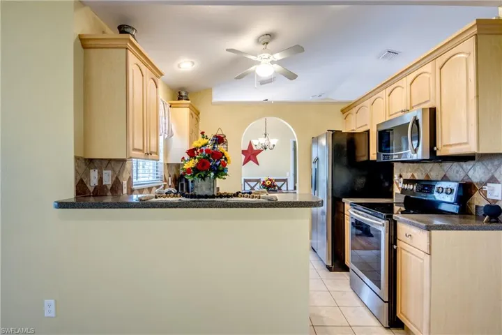 Cozy kitchen featuring light brown cabinetry, light tile flooring, kitchen peninsula, tasteful backsplash, and appliances with stainless steel finishes.