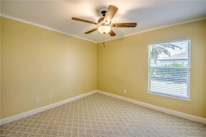 Guest bedroom with light colored farmhouse-style carpeting, plenty of natural light, beautiful view of landscaped back yard, crown molding, and smart home capable ceiling fan.