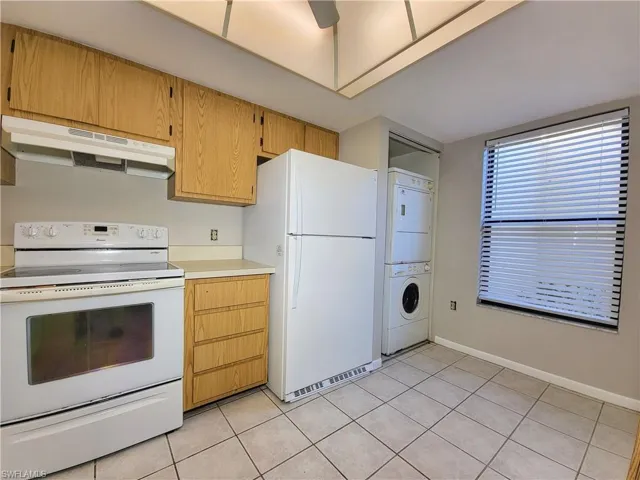 Kitchen featuring stacked washer / dryer, ceiling fan, light tile patterned floors, and white appliances