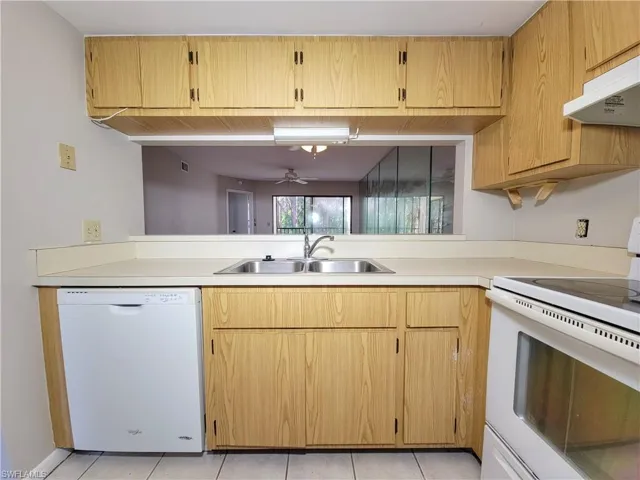 Kitchen with sink, light tile patterned flooring, white appliances, and ventilation hood