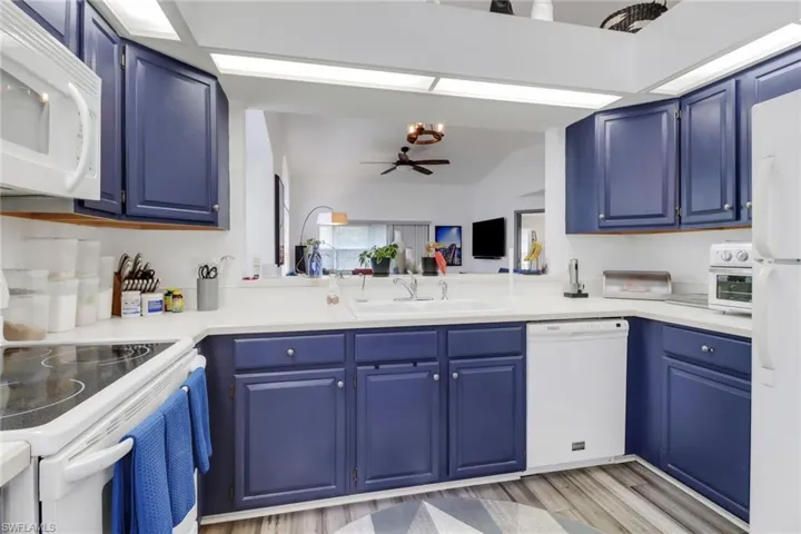 Kitchen featuring white appliances, sink, light wood-type flooring, ceiling fan, and blue cabinetry