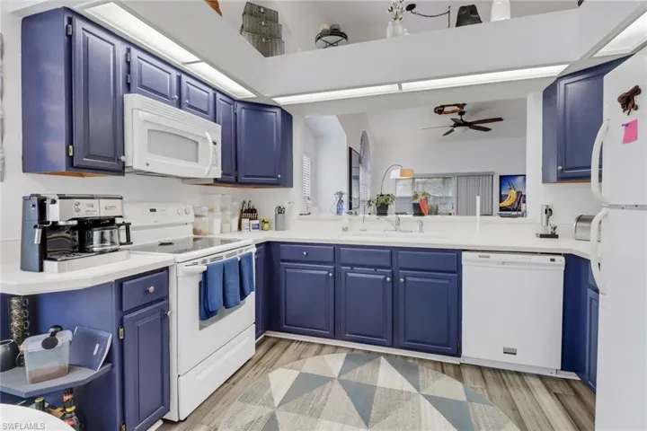 Kitchen featuring white appliances, kitchen peninsula, light wood-type flooring, blue cabinets, and ceiling fan