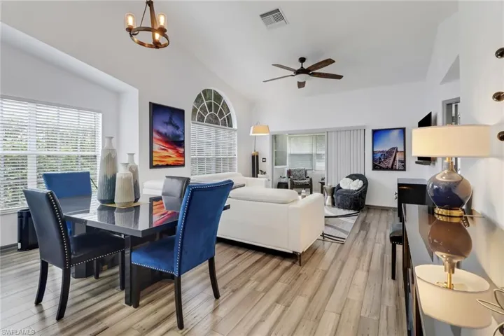 Dining area with light hardwood / wood-style floors, ceiling fan with notable chandelier, and vaulted ceiling