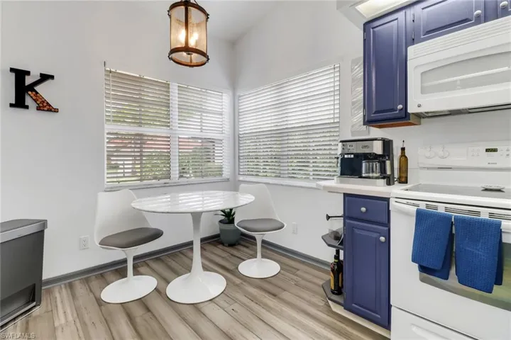 Kitchen with pendant lighting, white appliances, an inviting chandelier, blue cabinetry, and light hardwood / wood-style floors