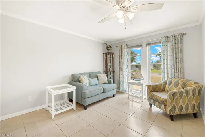 Living room with a ceiling fan, baseboards, ornamental molding, and light tile patterned floors