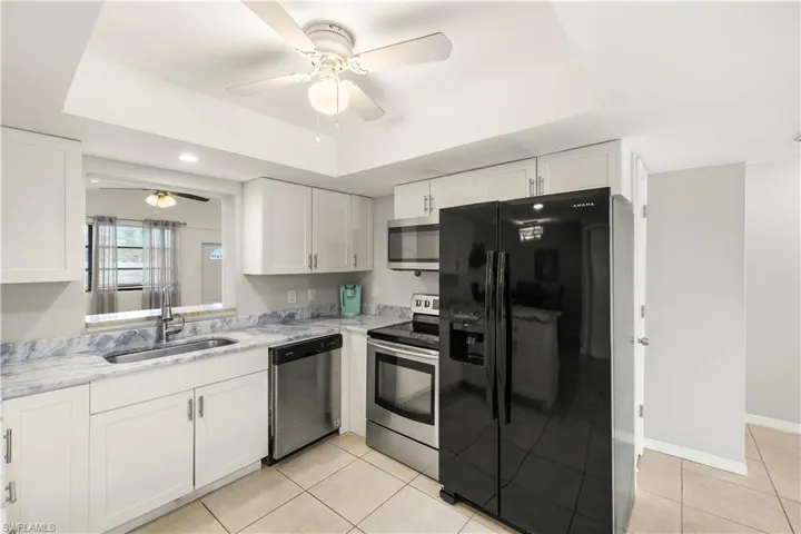 Kitchen featuring ceiling fan, a tray ceiling, a sink, light tile patterned floors, and stainless steel appliances