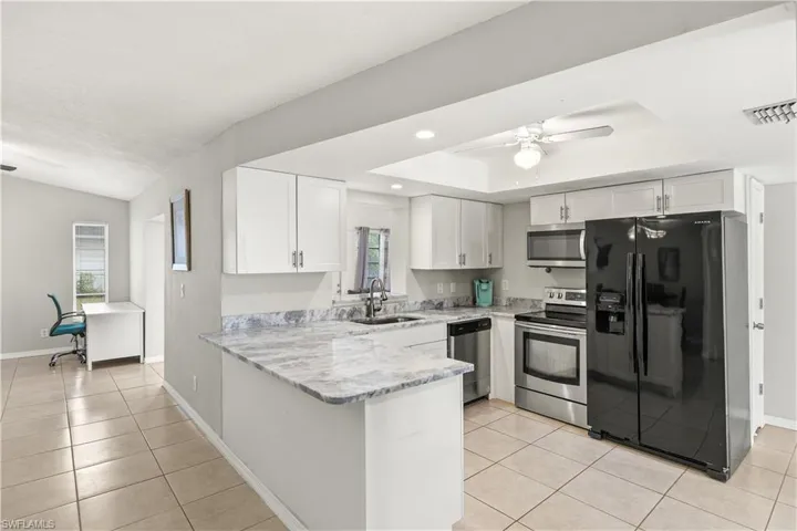 Kitchen with a sink, light tile patterned floors, white cabinets, and stainless steel appliances