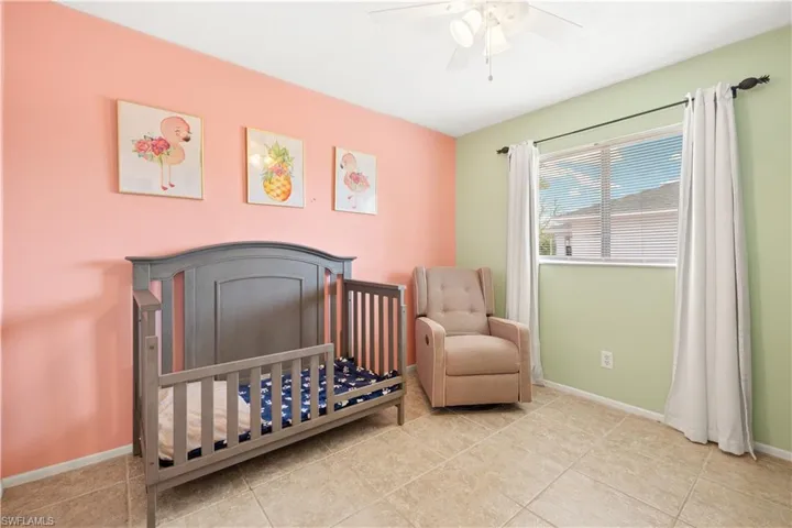 Bedroom featuring baseboards, a ceiling fan, a crib, and tile patterned flooring