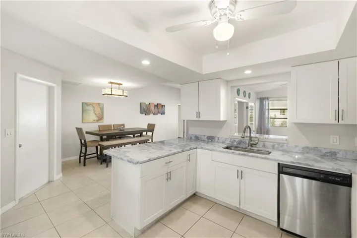 Kitchen with stainless steel dishwasher, a peninsula, a raised ceiling, white cabinetry, and a sink