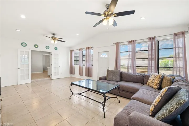Living room featuring light tile patterned floors, ceiling fan, french doors, and lofted ceiling