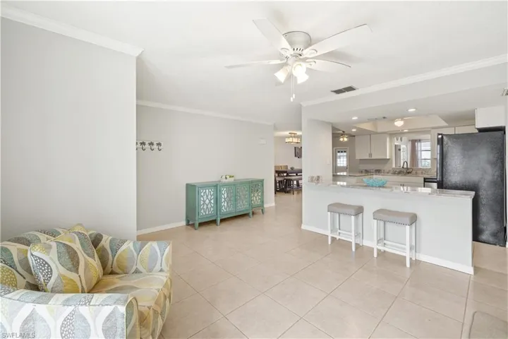 Living room with visible vents, ornamental molding, baseboards, a ceiling fan, and light tile patterned floors