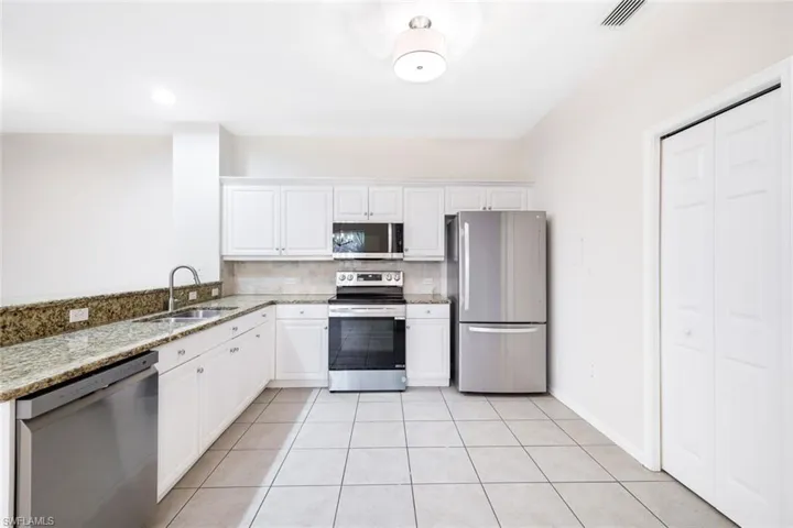 Kitchen featuring appliances with stainless steel finishes, light stone counters, sink, white cabinets, and light tile patterned flooring