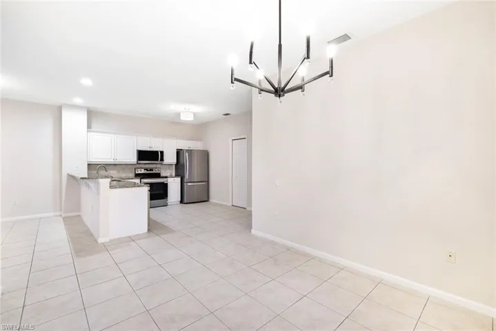 Kitchen with white cabinets, appliances with stainless steel finishes, tasteful backsplash, light stone counters, and kitchen peninsula