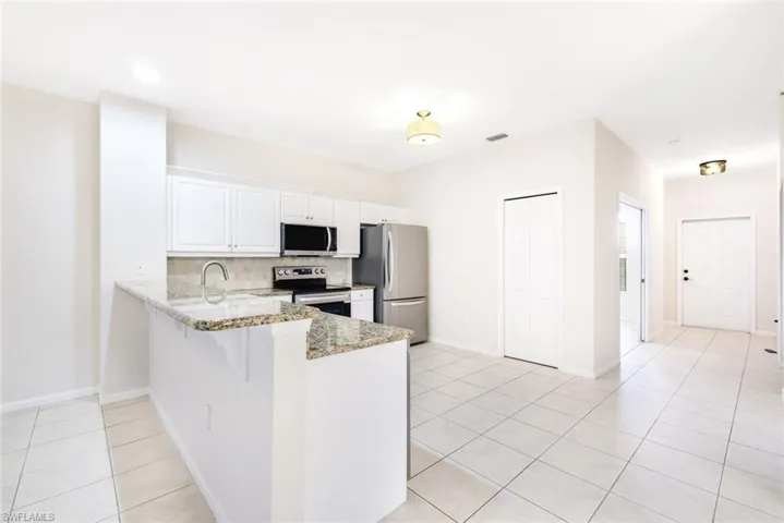 Kitchen featuring decorative backsplash, appliances with stainless steel finishes, light stone counters, light tile patterned floors, and white cabinets