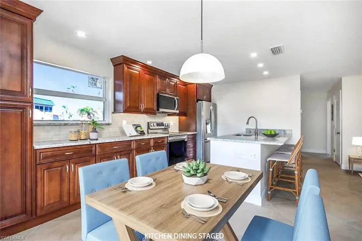 Kitchen featuring light tile patterned floors, stainless steel appliances, tasteful backsplash, hanging light fixtures, and a breakfast bar