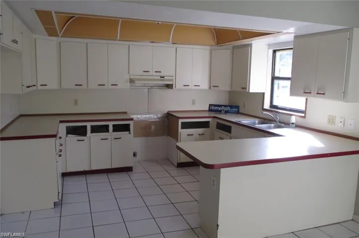 Kitchen with white cabinetry, a peninsula, light tile patterned flooring, light countertops, and under cabinet range hood