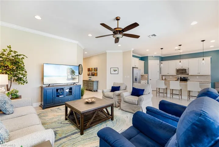Great room looking onto the kitchen and entryway. Features crown molding, recessed lighting, a ceiling fan, and light tile patterned floors wth plenty of room for seating.