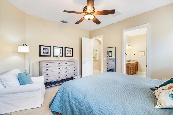 Primary Bedroom with ceiling fan, neutral colors, light colored carpet, ensuite bath.